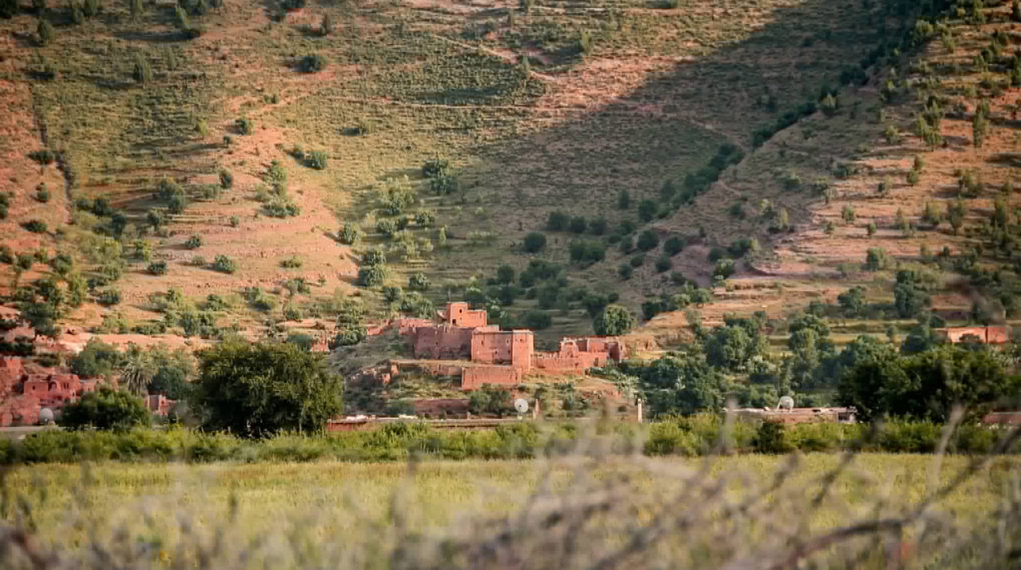 Village berbère en pisé ocre sur flanc de colline avec terrasses cultivées